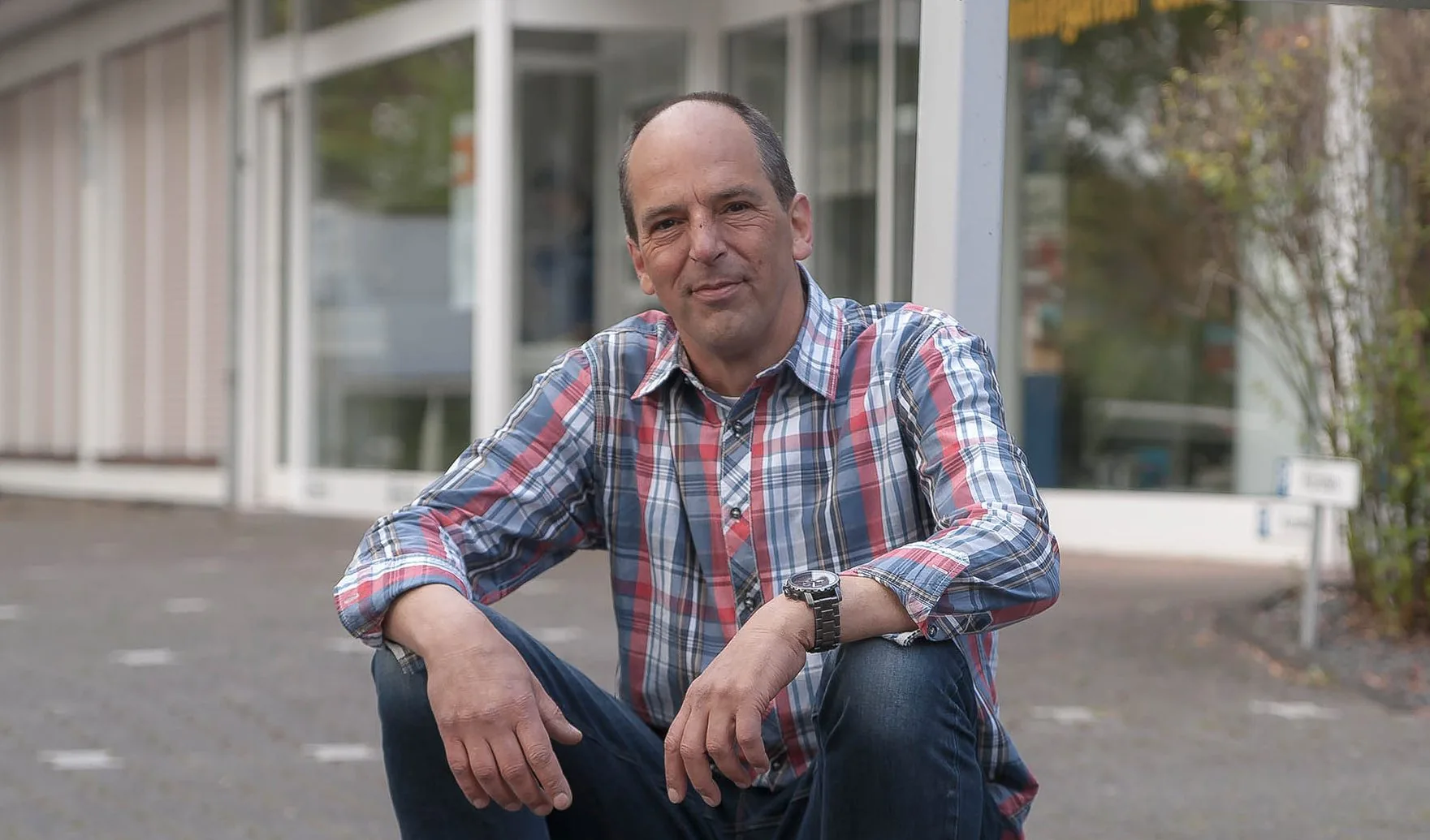 Andreas Müller in kariertem Hemd, sitzend vor dem Betriebsgebäude.