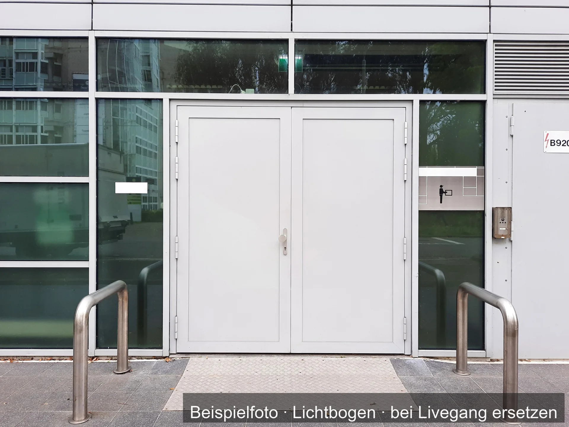 Eine hellgraue zweiflügelige Tür in einer Front aus Glas und Metall, davor zwei Bügel aus Edelstahl.
