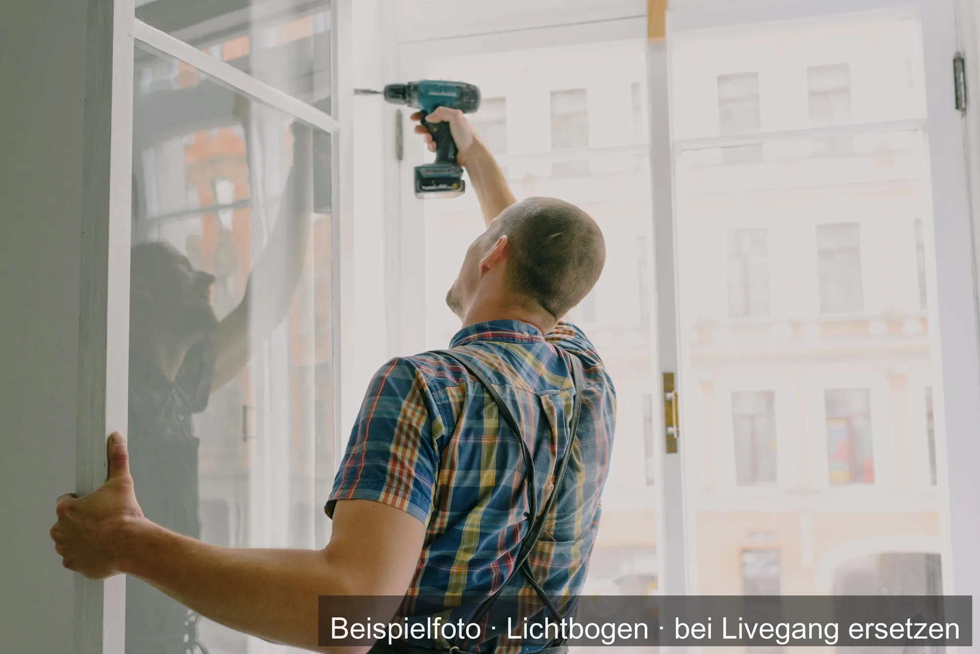 Ein Handwerker in kariertem Hemd setzt mit dem Akkuschrauber oben an einem geöffneten Fensterflügel an.