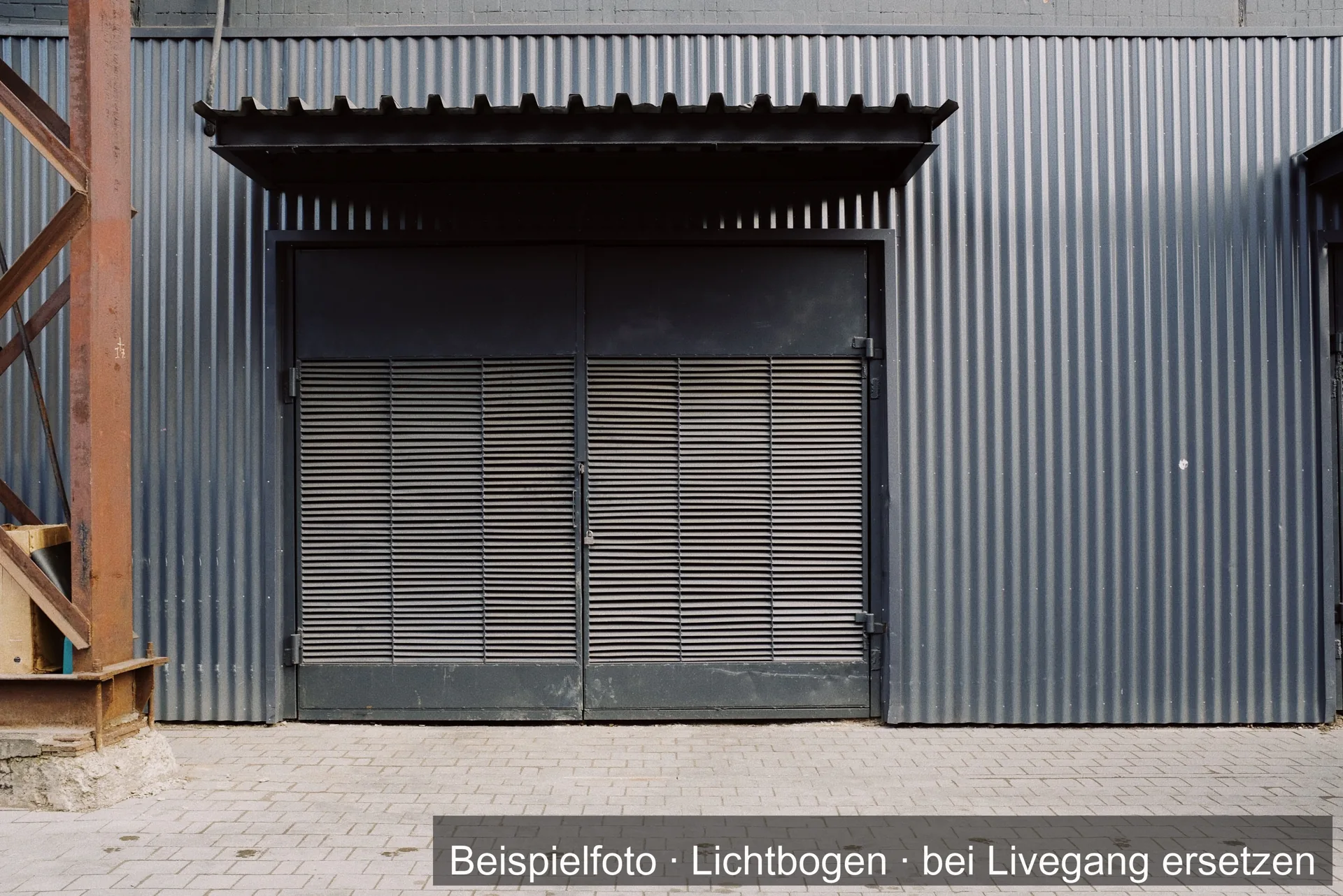 Ein zweiflügeliges Lamellentor aus Metall unter einem kleinen Vordach, eingelassen in eine graue Wellblechwand.